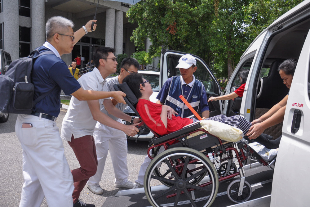 Volunteers assisting a wheelchair bound aid beneficiary to get off the car. (Photo by Peter Andrew)